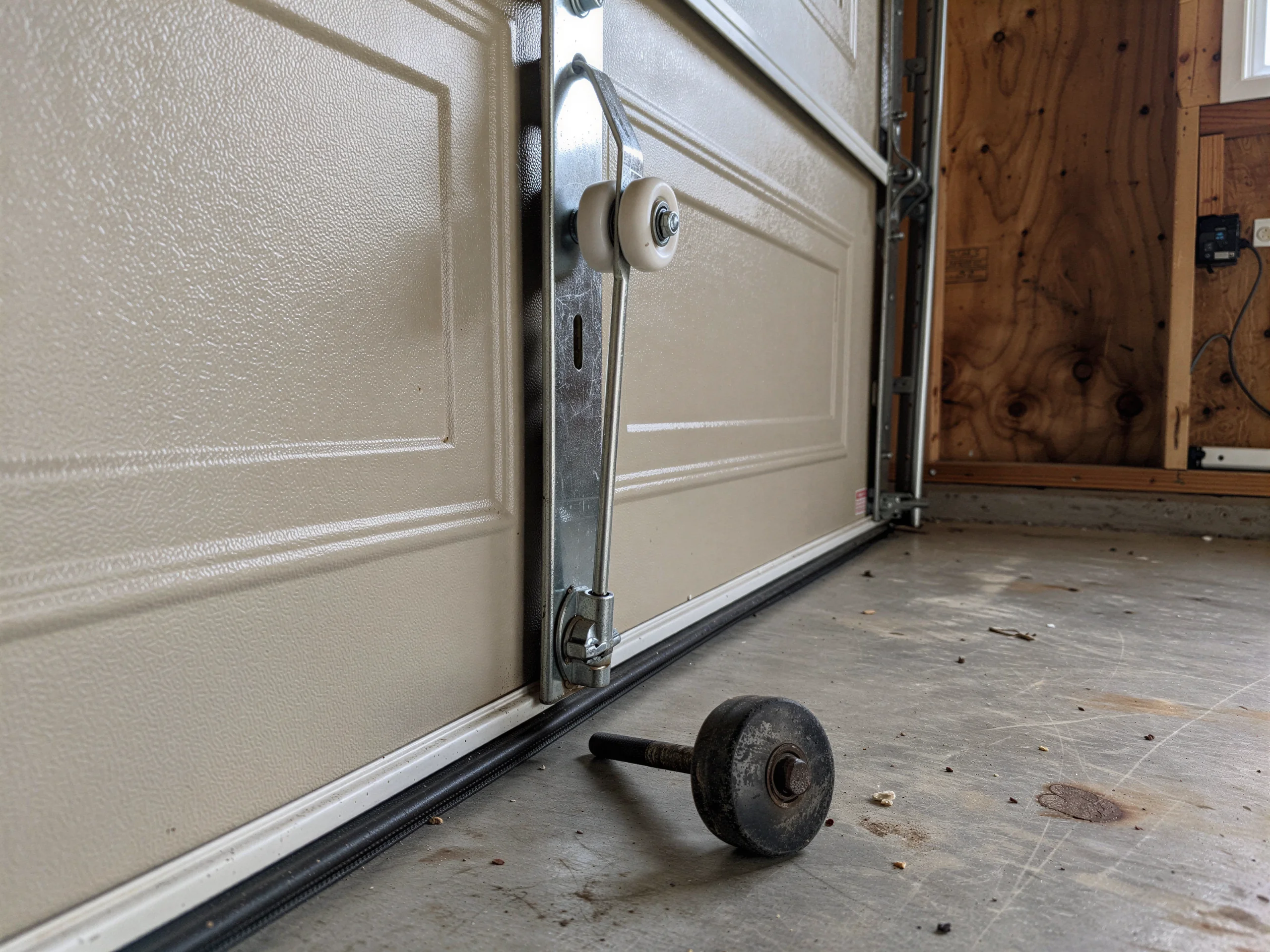 A garage door with a detached roller on the concrete floor.